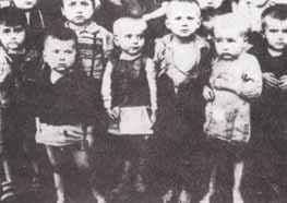 A black and white photo of young children standing closely together, dressed in simple, worn clothing.