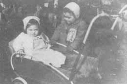 Two young children in vintage clothing sit in a stroller.